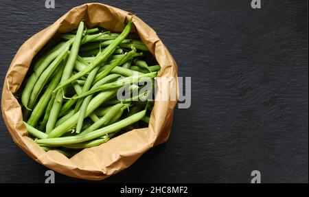 Fotografie von grünen Bohnen in einer braunen Papiertüte auf Schieferhintergrund für Menü, Etikett oder Schild /die grüne Bohne, auch grüne Bohne genannt, ist eine Vielzahl von fle Stockfoto