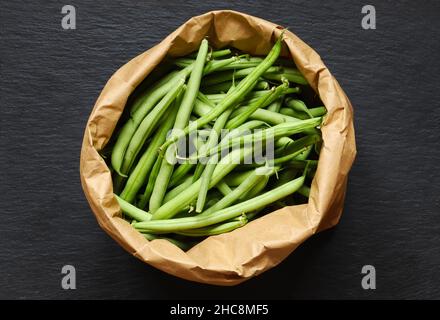 Fotografie von grünen Bohnen in einer braunen Papiertüte auf Schieferhintergrund für Lebensmittelillustrationen /die grüne Bohne, auch grüne Bohne genannt, ist eine Vielzahl von Gewehren Stockfoto