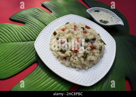 Leckeres indisches Frühstück mit Gemüse-Upma, serviert mit Kokosnuss-Chutney auf grünem Blatt. südindisches gesundes Frühstück aus rava oder Grieß mit Chopp Stockfoto