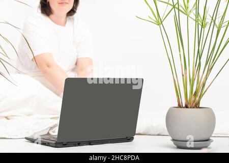 Frau arbeitet mit einem Laptop, der auf dem Boden in der Nähe von Zimmerpflanzen sitzt. Arbeiten Sie zu Hause. Stockfoto