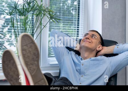 Der junge Regisseur ruht in seinem Büro und legt seine Füße auf den Tisch. Der Manager reflektiert über die Arbeit Stockfoto