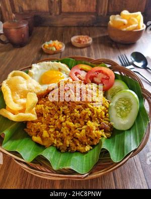 Gebratener indonesischer Reis mit sonniger Seite nach oben, Tomaten- und Gurkenscheiben, Gurken, Gurken, gebratene Schalotten und Cracker auf einem Holztisch Stockfoto
