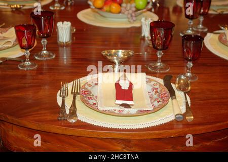 Elegante Platzgestaltung, Weihnachtsmann Dekoration, porzellanteller, goldfarbene Utensilien, rote Kelche, Holztisch, Feiertag, festlich, Weihnachten, Winterthur Museum, De Stockfoto