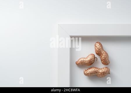 Weiß gerahmte minimalistische Komposition aus goldenen Erdnüssen auf weißem Hintergrund mit Platz für Text. Stockfoto