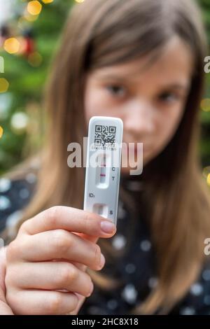 Details zur geringen Schärfentiefe (selektiver Fokus) mit den Händen eines 9-jährigen Mädchens, das einen COVID-19 Antigen Rapid Test hält, mit einem positiven Ergebnis. Stockfoto