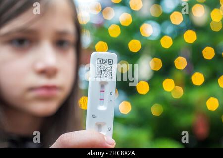 Details zur geringen Schärfentiefe (selektiver Fokus) mit den Händen eines 9-jährigen Mädchens, das einen COVID-19 Antigen Rapid Test hält, mit einem positiven Ergebnis. Stockfoto