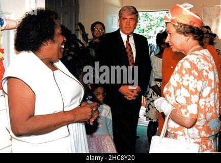 Frau Alice Frazier, links, begrüßt Königin Elizabeth II. Von Großbritannien, rechts, in ihrem Haus in Washington, DCs Drake Place, wie der US-amerikanische Minister für Wohnungsbau und Stadtentwicklung Jack Kemp, Mitte, am 15. Mai 1991 anschaut. Drake Place ist eine Gruppe von neuen, bezahlbaren Wohnungen, die gemeinsam von staatlichen und privaten Interessen finanziert werden. Die Königin ist auf einem 12-tägigen offiziellen Besuch in den USA. Kredit: Ron Thomas / Pool über CNP Stockfoto