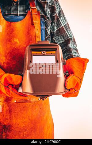Arbeiter in der Schwerindustrie in Schutzanzug, Handschuhe, hält eine Schutzmaske unter seinem Arm, Nahaufnahme, vertikales Foto, Feurige Farben Stockfoto