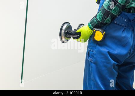 Ein Glasarbeiter hält mit einem speziellen Sauger eine dicke Glasscheibe in den Händen Stockfoto