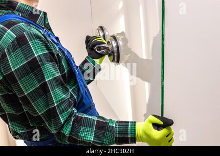 Ein Glasarbeiter hält mit einem speziellen Sauger eine dicke Glasscheibe in den Händen Stockfoto