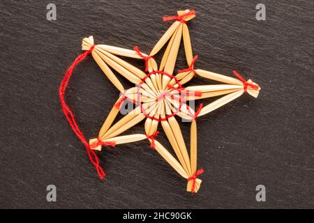 Ein Weihnachtsspielzeug aus Stroh in Sternform auf einem Schieferstein, Nahaufnahme, Draufsicht.