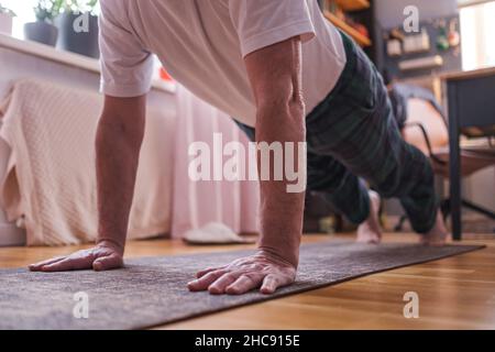 Fröhlicher älterer hispanischer Mann, der eine Seitenplankenübung im Wohnzimmer macht. Stockfoto
