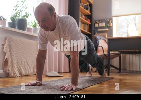 Fröhlicher älterer hispanischer Mann, der eine Seitenplankenübung im Wohnzimmer macht. Stockfoto