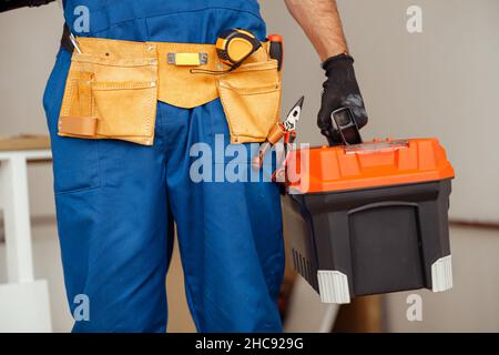 Nahaufnahme eines Mitarbeiters des Auftragnehmers in Overalls, der den Werkzeugkasten hält, während er im Gebäude steht Stockfoto