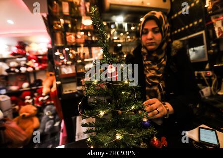 Gaza, Palästina. 26th Dez 2021. In Gaza City arbeitet eine Palästinenserin an ihrem Geschenkeladen.Geschenkeläden und Restaurants bereiten sich im Gazastreifen darauf vor, Weihnachten zu feiern, indem sie ihre Restaurants dekorieren und Geschenke in ihren Geschäften wie Weihnachtsmannpuppen und kleine leuchtende Weihnachtsbäume ausstellen. Kredit: SOPA Images Limited/Alamy Live Nachrichten Stockfoto