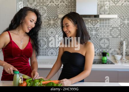 Zwei Frauen, die in formeller Kleidung gekleidet in der Küche zusammenstehen und Gemüse hacken Stockfoto