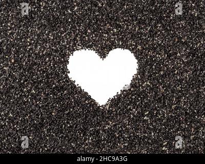 Leere Herzform in der Mitte von schwarzem Sand oder Holzkohle Textur. Makroaufnahme. Abstrakter Hintergrund mit weißem Symbol für Liebe, Fürsorge und Romantik. Stockfoto