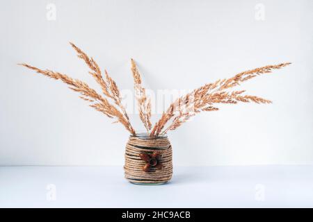 Spikeletts in handgefertigter Vase auf dem Tisch, weißer Hintergrund, Herbstkonzept. Nahaufnahme. Stockfoto