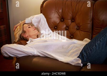 Glücklich verträumte Frau liegt auf Leder braun Sofa zu Hause im Zimmer Stockfoto