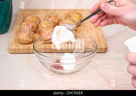 Ein Mann legt saure Creme zum Gießen, um faule Kohlrollen in einem langsamen Herd zu kochen. Stockfoto