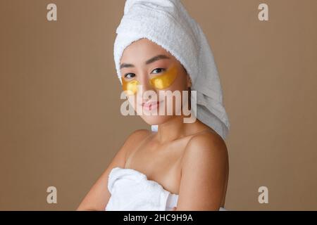 Junge Frau mit Masken unter den unteren Augenlidern, die im Studio stehen Stockfoto