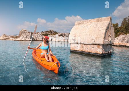 Mädchen auf einem Kajak erkundet ein uraltes lykisches Grab, das mitten in einer überfluteten Stadt nach einem schweren Erdbeben in der Nähe der Insel Kekova aus dem Wasser ragt Stockfoto