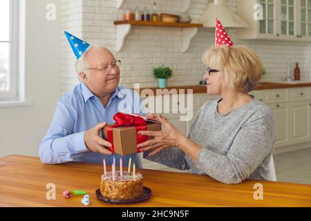 Glückliches Seniorenpaar in Partyhüten, das zu Hause den Geburtstag seiner Frau oder den Geburtstag seiner Frau feiert Stockfoto