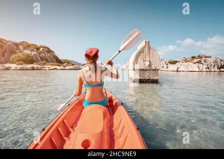 Mädchen auf einem Kajak erkundet ein uraltes lykisches Grab, das mitten in einer überfluteten Stadt nach einem schweren Erdbeben in der Nähe der Insel Kekova aus dem Wasser ragt Stockfoto