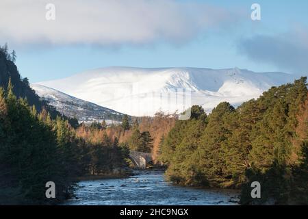 Ein Blick entlang des Flusses Dee auf dem Balmoral Estate, in der Nähe von Braemar, in Richtung der Alten Brücke von Dee, mit schneebedeckten Hügeln und Bergen im Hintergrund Stockfoto