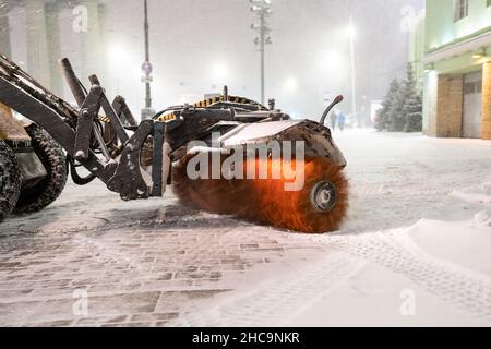Traktor mit rotierendem Besen, der die Stadt nach Schneefall von Schnee und Eis freiräumt. Winterdienst Stockfoto