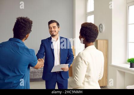 Freundlicher männlicher Immobilienmakler, der die Hände schüttelt und junge Familie in neuem Zuhause begrüßt. Stockfoto