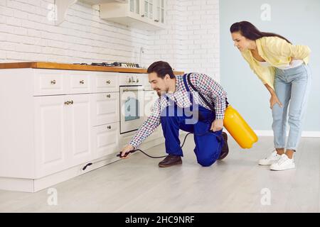 Schädlingsbekämpfungsdienstmitarbeiter sprühen Kakerlakeninsektizid unter Küchenschränke Stockfoto