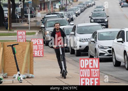 Austin, Texas, USA. 26th. Dezember 2021. Ein Mann auf einem Roller fliegt an einem mobilen privaten COVID-Testgelände vorbei, das von Bewohnern überfordert ist, die während der Ferien getestet werden möchten. Gäste meldeten bis zu zwei Stunden Wartezeit am Drive-Through-Standort, einer von mehreren wurde über die Weihnachtsfeiertage eröffnet. Kredit: Bob Daemmrich/Alamy Live Nachrichten Stockfoto