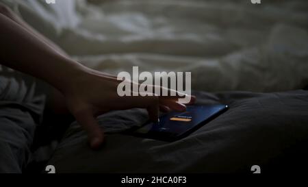 Nahaufnahme eines schlafenden Mannes, der durch sein Telefon auf dem Bett liegend geweckt wurde. Männliche Hand versuchte, den Wecker auszuschalten, der in der Nähe auf einer Decke zu Hause lag Stockfoto