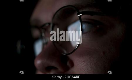 Brille mit reflektiertem Computerbildschirm in Linsen. Nahaufnahme eines durchdachten Geschäftsmannes oder eines fokussierten Studenten, der spät in der Nacht auf Schwarz isoliert arbeitet Stockfoto