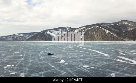 Winter Baikalsee mit Touristen auf Eis Spaß haben. Luftaufnahme von Menschen, die die wilde Natur des gefrorenen Sees auf bewölktem Himmel erkunden. Stockfoto
