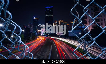 Nachtansicht einer Stadt mit verschwommenen Autolichtern in Bewegung, die durch den Zaun gesehen werden Stockfoto