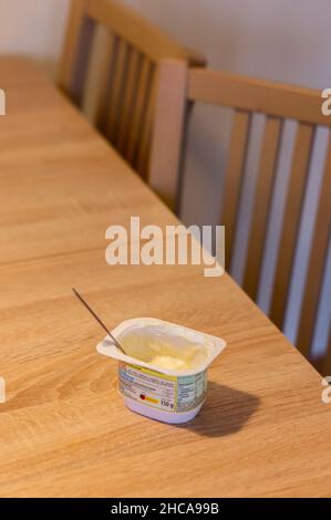 Fast leere geöffnete Tasse mit Vanilledessert und Löffel auf einem Tisch am Abend. Stockfoto