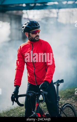 Seitenansicht eines jungen coolen Radfahrers in roter Sportkleidung, der an einem düsteren Tag ein Fahrrad fährt Stockfoto
