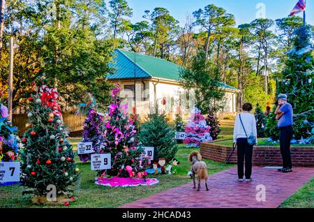 Ein Paar geht mit seinem Hund an geschmückten Weihnachtsbäumen am Water Tower Plaza am 24. Dezember 2021 in Dauphin Island, Alabama, vorbei. Stockfoto
