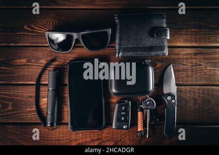 Draufsicht auf EDC oder Alltagsgegenstände des modernen Stadtmenschen: Klappmesser, Geldbörse, Telefon, Schlüssel, Taschenlampe und Sonnenbrille. Stockfoto
