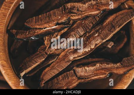 Geschnitten auf Stücke Ling Zhi Natural Chinese Herb oder Reishi Pilz, Ganoderma in Holzplatte Nahaufnahme von oben. Bio-Kräutermedizin Stockfoto