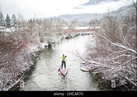 Ein Paddelboarder paddelt während eines Schneesturms einen kanadischen Fluss hinauf. Whistler, BC, Kanada. Stockfoto