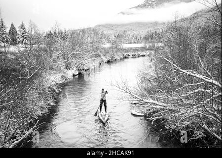 Ein Paddelboarder paddelt während eines Schneesturms einen kanadischen Fluss hinauf. Whistler, BC, Kanada. Stockfoto