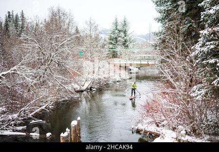 Ein Paddelboarder paddelt während eines Schneesturms einen kanadischen Fluss hinauf. Whistler, BC, Kanada. Stockfoto