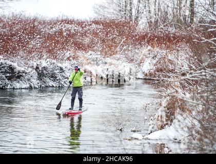 Ein Paddelboarder paddelt während eines Schneesturms einen kanadischen Fluss hinauf. Whistler, BC, Kanada. Stockfoto