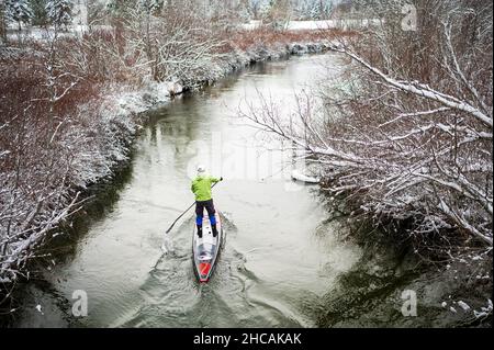 Ein Paddelboarder paddelt während eines Schneesturms einen kanadischen Fluss hinauf. Whistler, BC, Kanada. Stockfoto