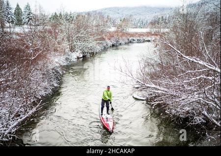 Ein Paddelboarder paddelt während eines Schneesturms einen kanadischen Fluss hinauf. Whistler, BC, Kanada. Stockfoto