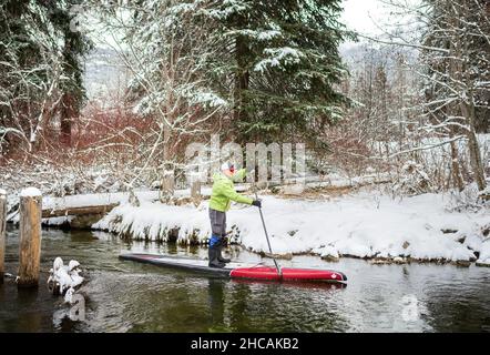 Ein Paddelboarder paddelt während eines Schneesturms einen kanadischen Fluss hinauf. Whistler, BC, Kanada. Stockfoto