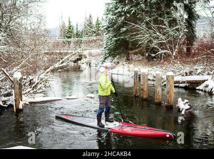 Ein Paddelboarder paddelt während eines Schneesturms einen kanadischen Fluss hinauf. Whistler, BC, Kanada. Stockfoto